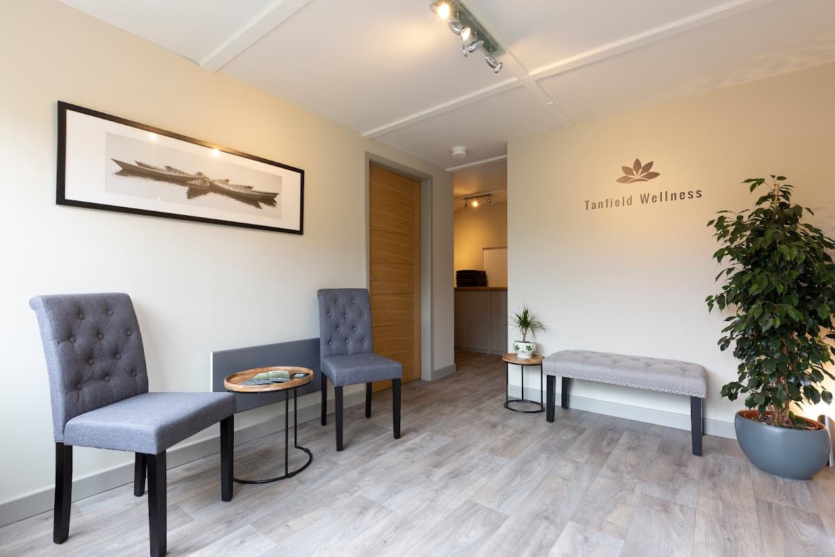 Welcoming interior of Tanfield Wellness with two gray chairs, a small table, a plant, and a framed artwork on the wall.