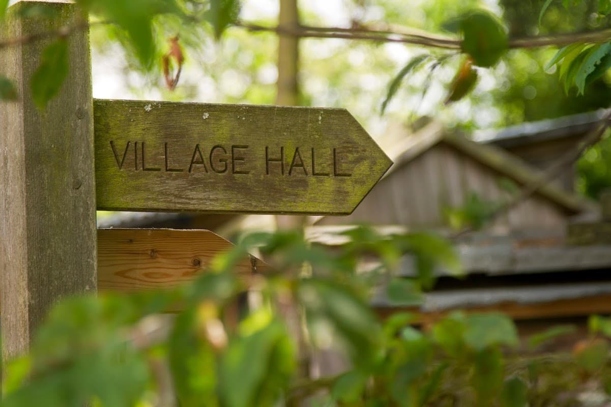Wooden sign pointing to "Village Hall" surrounded by greenery in Westerdale, Yorkshire.