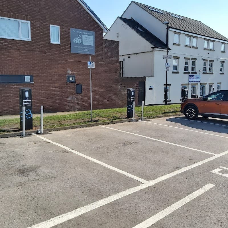 Free parking area with numbered spaces, adjacent buildings, and a parked orange car under clear blue skies.