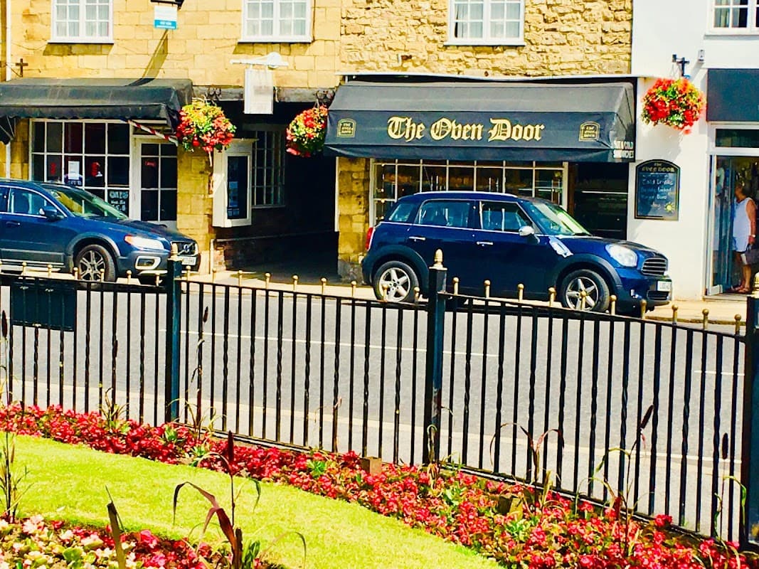 The Oven Door Bakery sign with flower baskets and cars parked outside, set in a picturesque street in Wetherby.