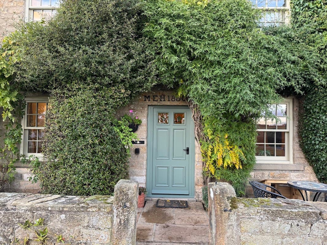 Charming stone farmhouse entrance, adorned with lush greenery and a light blue door, surrounded by a quaint stone wall.