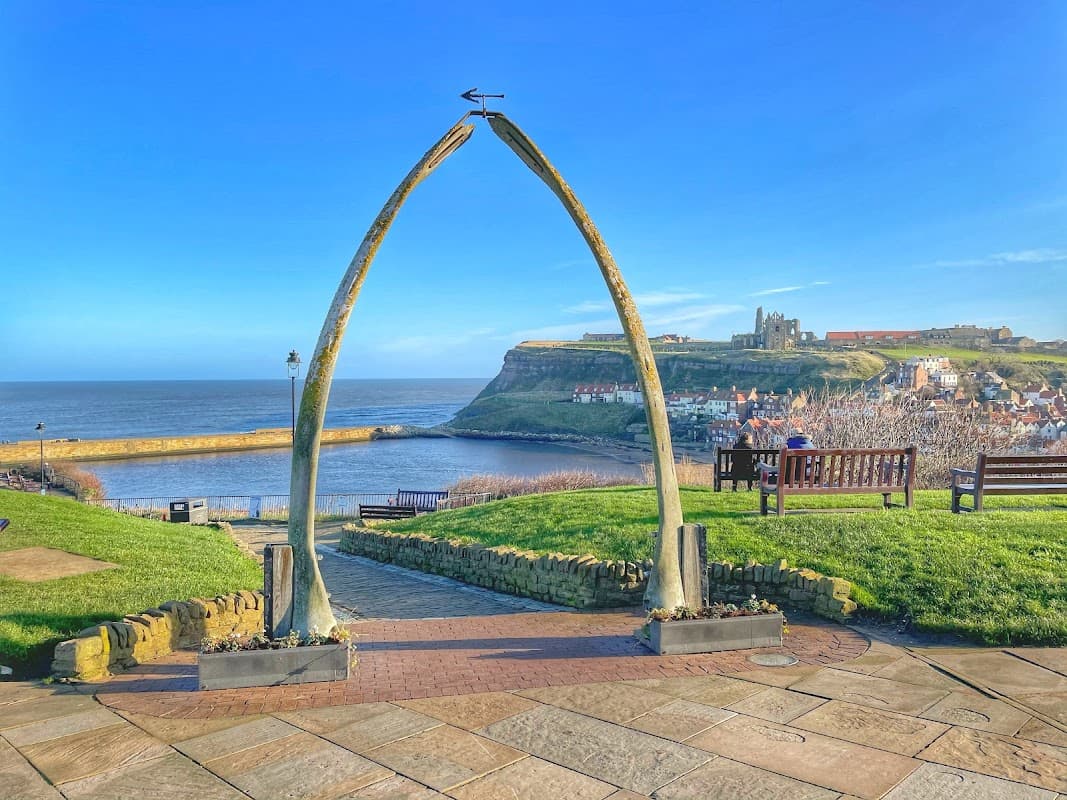 Whalebone Arch framed by green grass, with a view of Whitbyβs coastline and historic buildings in the background.
