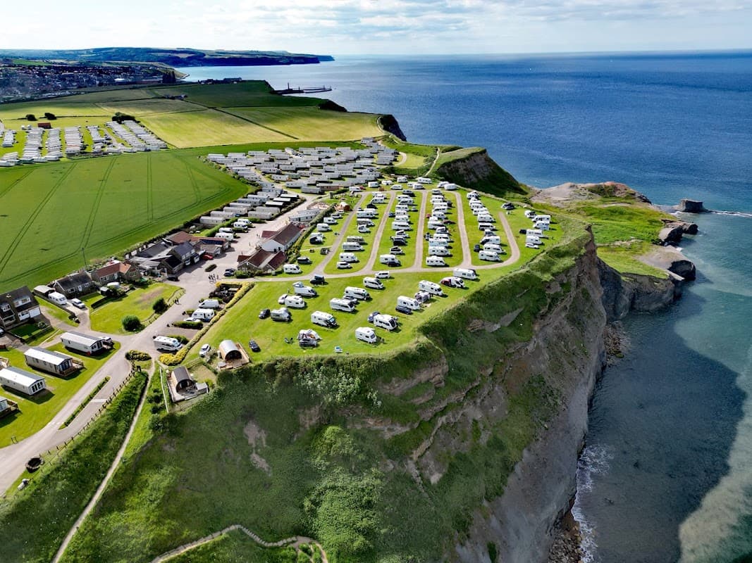 Aerial view of Whitby Holiday Park featuring caravans, green fields, and cliffs overlooking the sea.