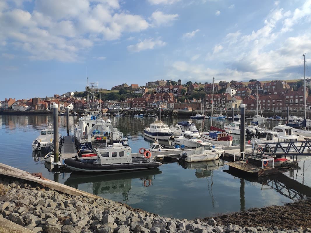 Pay & Display parking sign with boats and a scenic harbor view in Whitby, Yorkshire, under a partly cloudy sky.