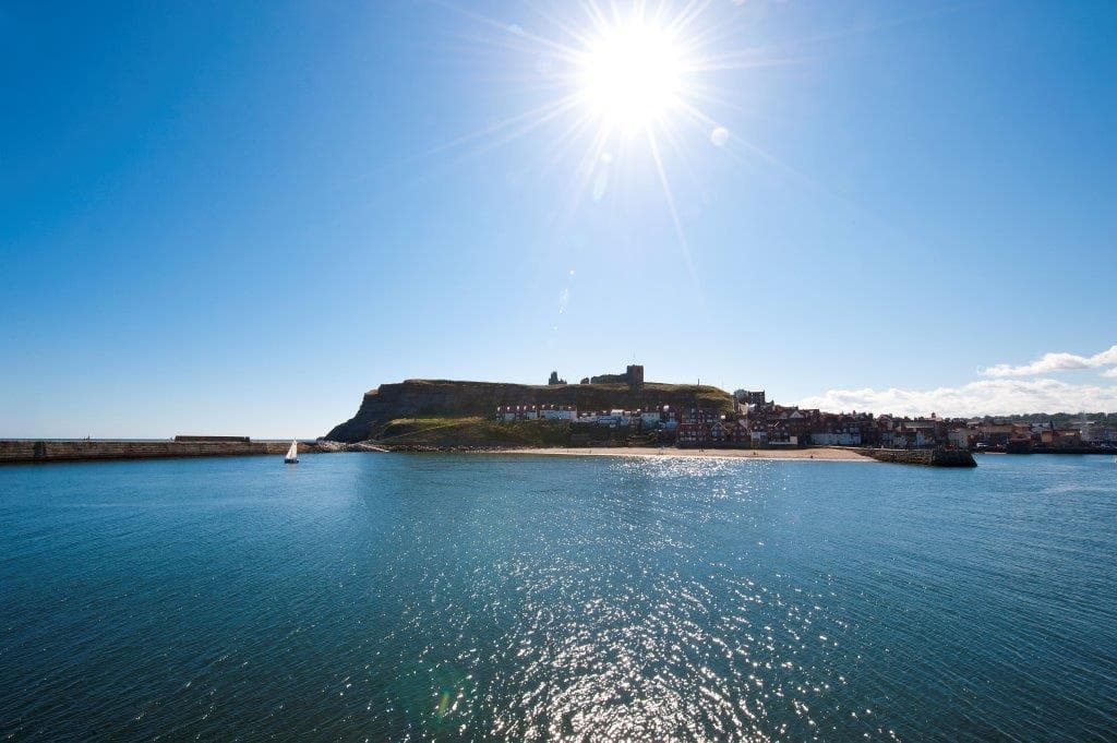 Bright sun over Whitby, with a view of the coastline and historic buildings along the water.