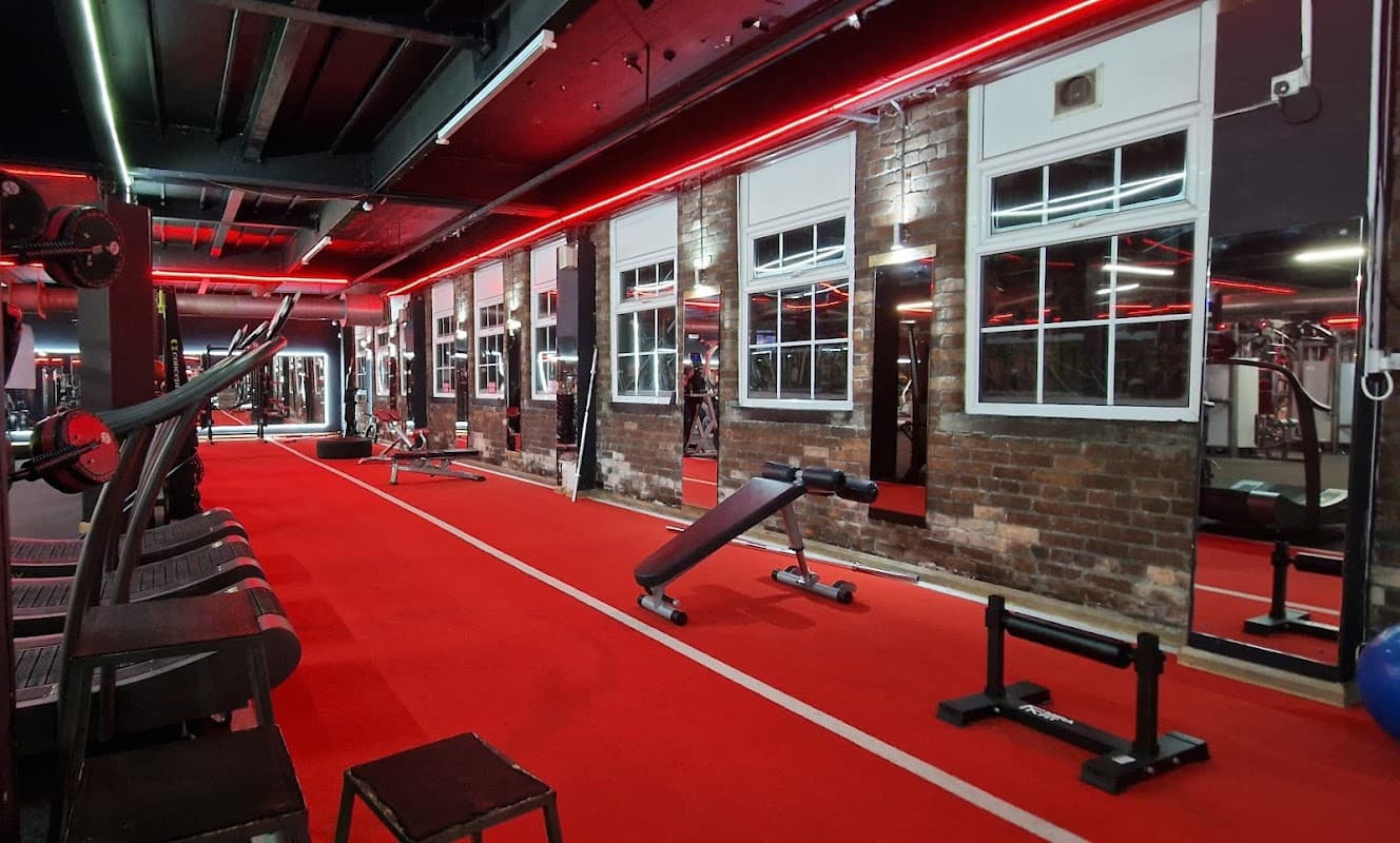 Modern gym interior with red lighting, exposed brick walls, workout equipment, and a vibrant red carpeted floor.