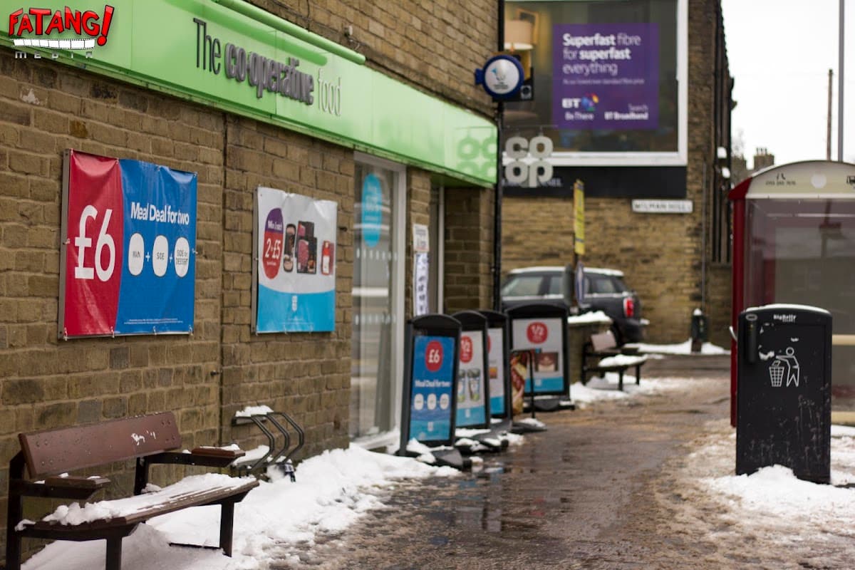 Co-op Food storefront in Wibsey, Yorkshire, with benches, snow, and promotional signs visible.