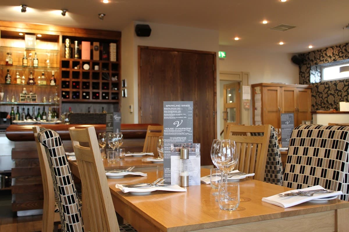 Stylish dining area with wooden tables, chairs, wine bottles on shelves, and menus displayed at The Olive Lounge Ltd.