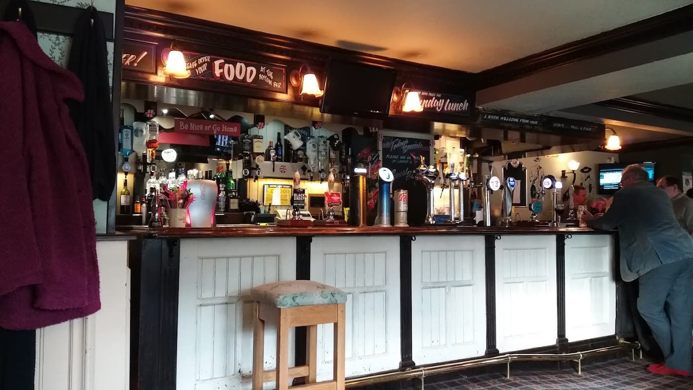 Wooden bar with various beer taps, illuminated signs, and patrons enjoying drinks in a cozy pub setting.