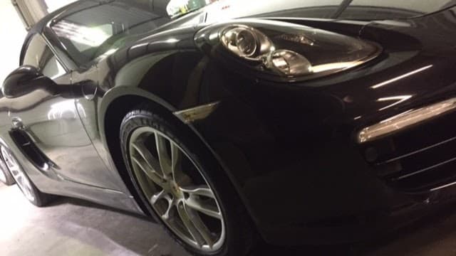 Sleek black sports car parked in a garage, showcasing shiny alloy wheels and detailed headlights.