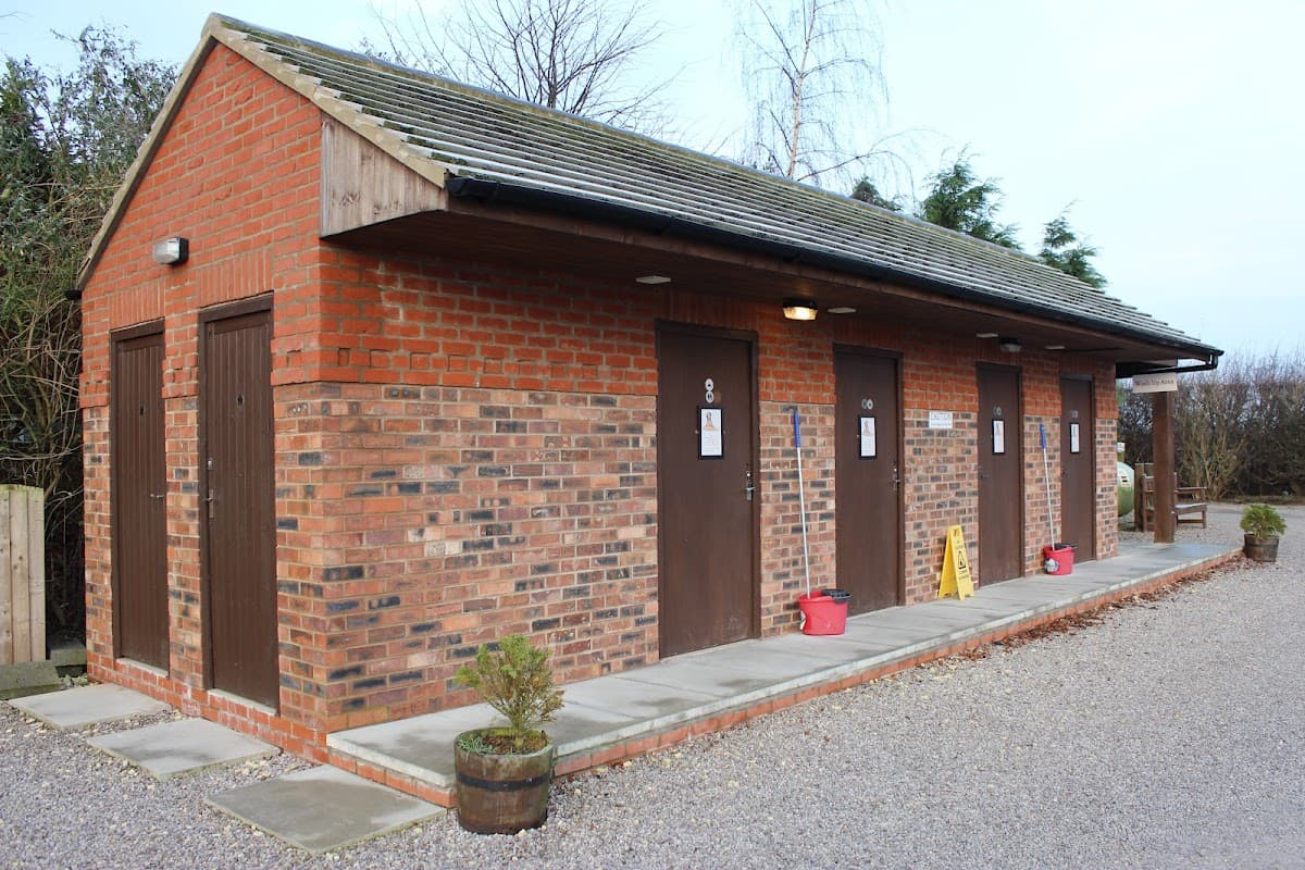 Red brick building with four doors, gravel path, and potted plants outside, set in a green landscape.