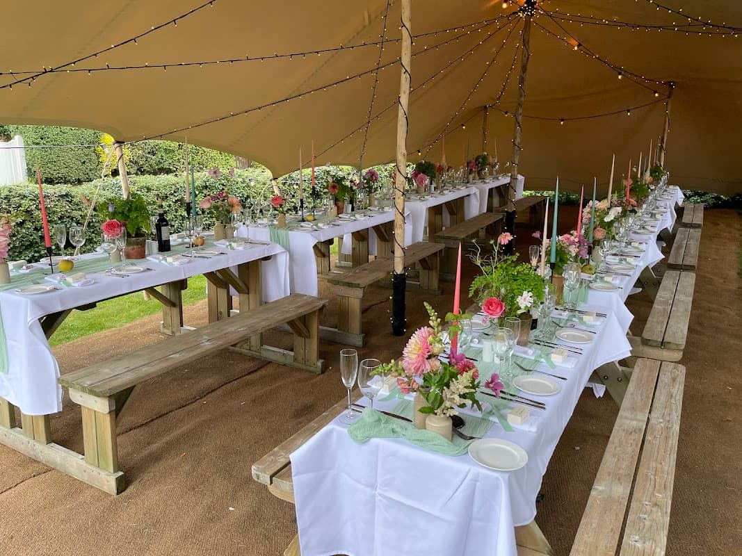 Festively arranged outdoor dining area with long tables, floral centerpieces, candles, and twinkling lights.