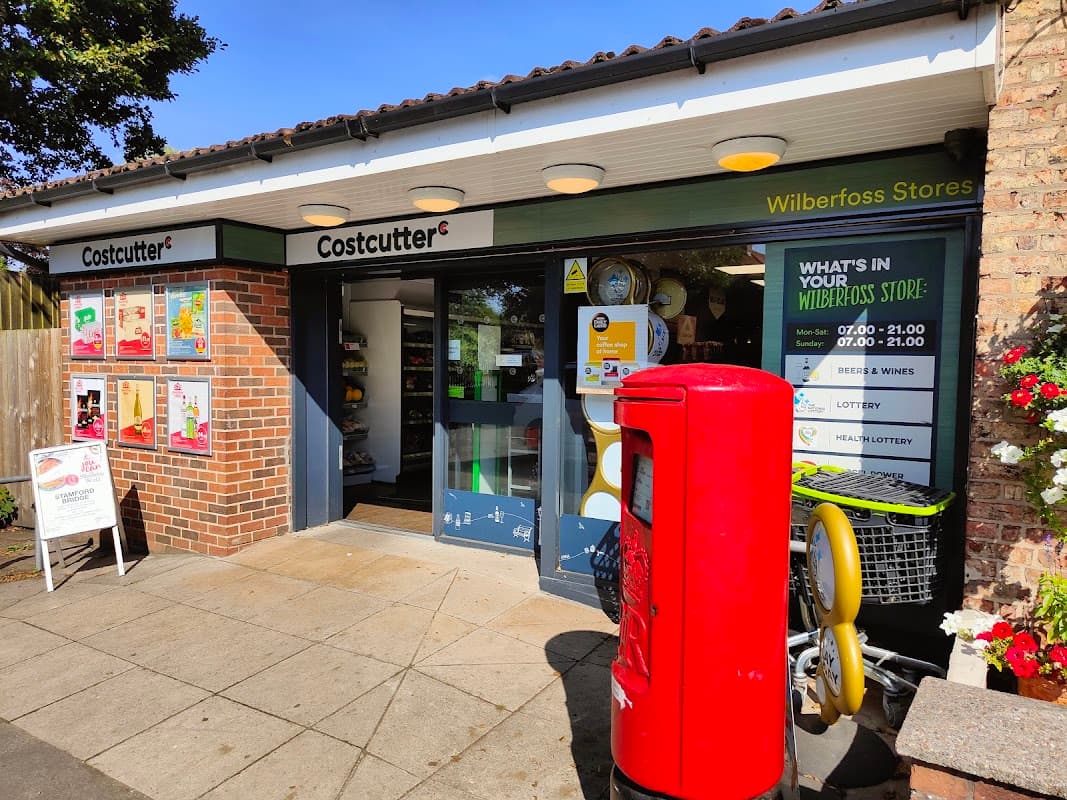Costcutter store entrance with signage, lottery display, and a red post box outside in Wilberfoss, Yorkshire.