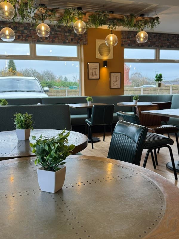 Cozy bistro interior with wooden tables, green plants, and pendant lights, overlooking a scenic view.