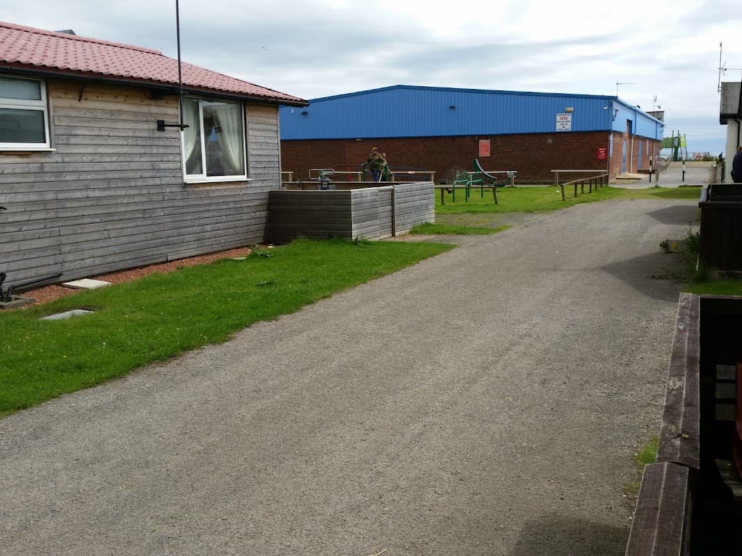 Beachside chalets with a gravel path, grassy areas, and nearby blue commercial building in Wilsthorpe, Yorkshire.