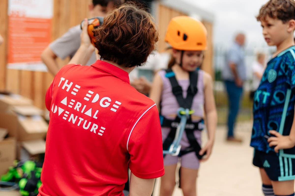 A staff member in a red shirt assists children in harnesses, preparing for an aerial adventure at The Edge in Yorkshire.