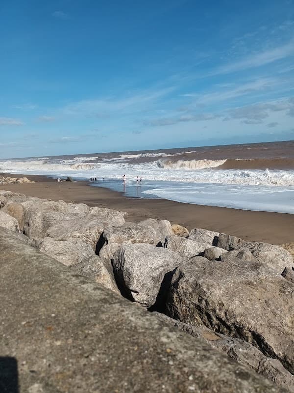 View of a sandy beach with waves crashing, rocky foreground, and a clear blue sky in Withernsea, Yorkshire.