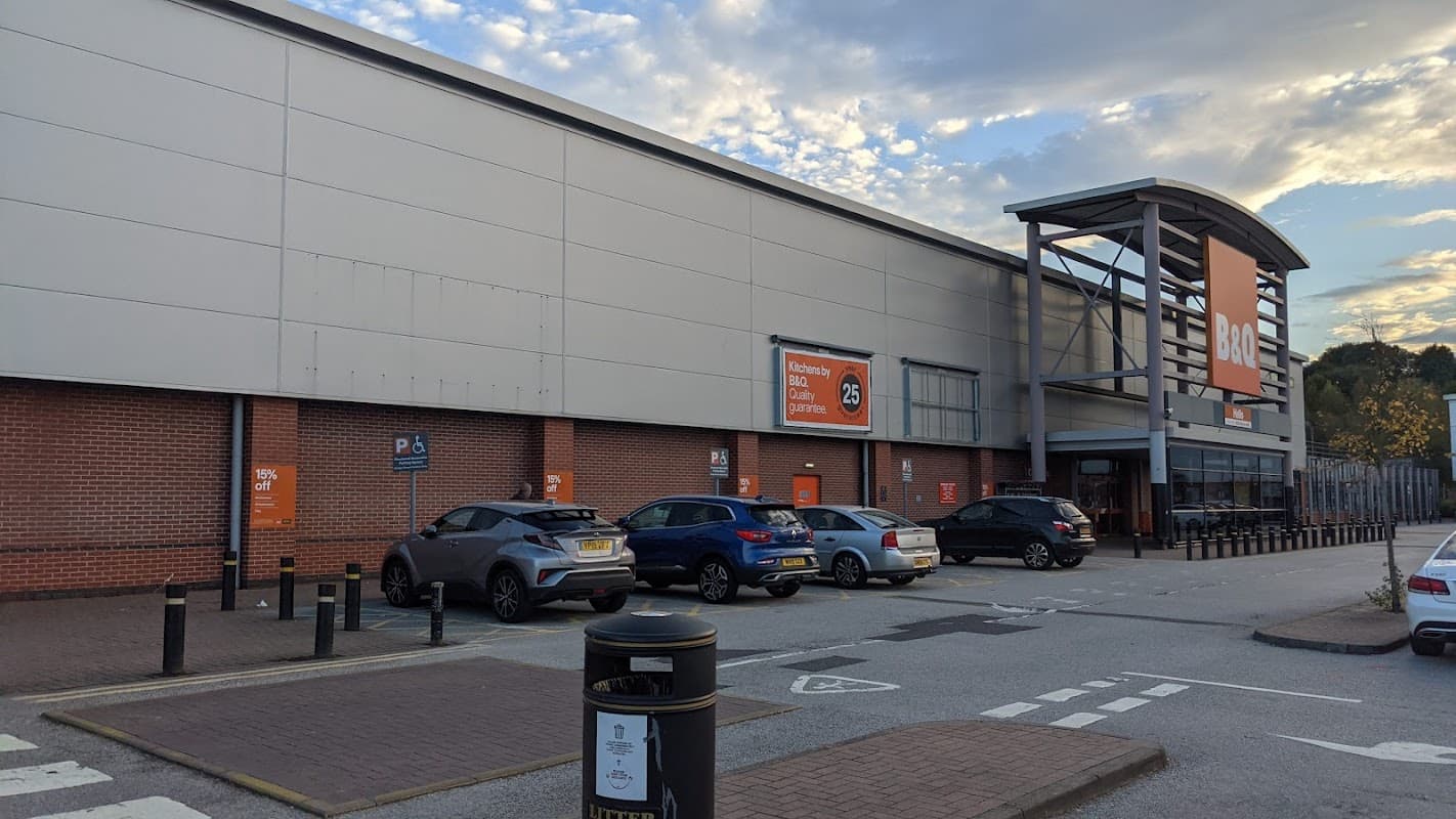 B&Q store exterior with large signage, parking area, and several cars parked in front under a cloudy sky.