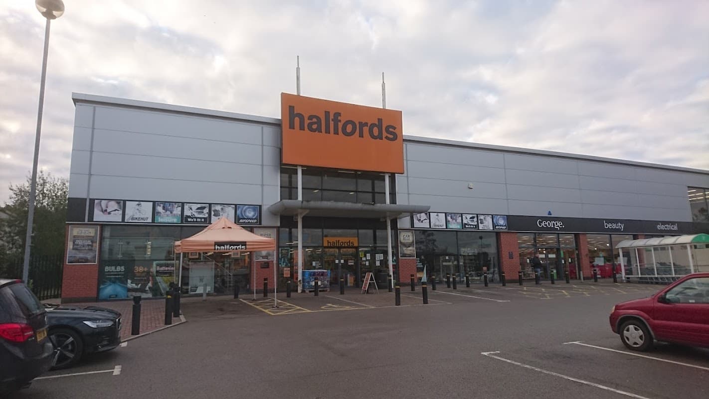 Halfords store exterior with large orange signage, parking area, and various shopfronts in Wombwell, Yorkshire.