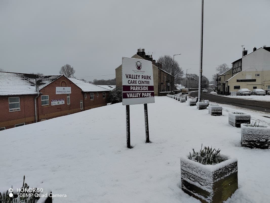 Snow-covered landscape with a sign for Valley Park Care Centre and nearby buildings in Wombwell, Yorkshire.