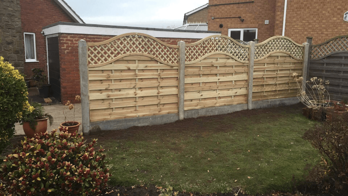 Wooden fence with decorative lattice top, surrounded by a garden with potted plants and a well-maintained lawn.