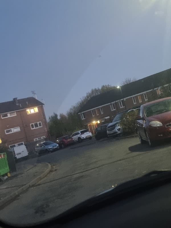 Car park with parked vehicles, residential buildings in the background, and a dusky sky in Woodhouse, Yorkshire.