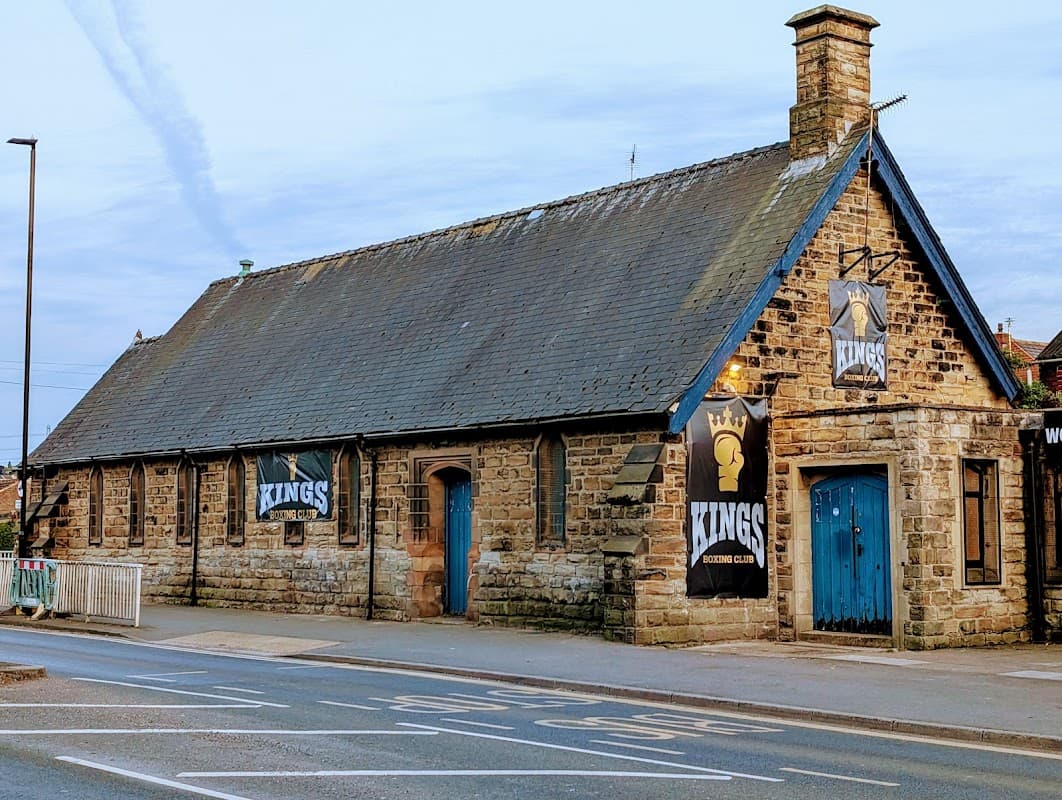 Historic stone building with blue doors and banners for "Kings" on the exterior, set along a street in Woodhouse.