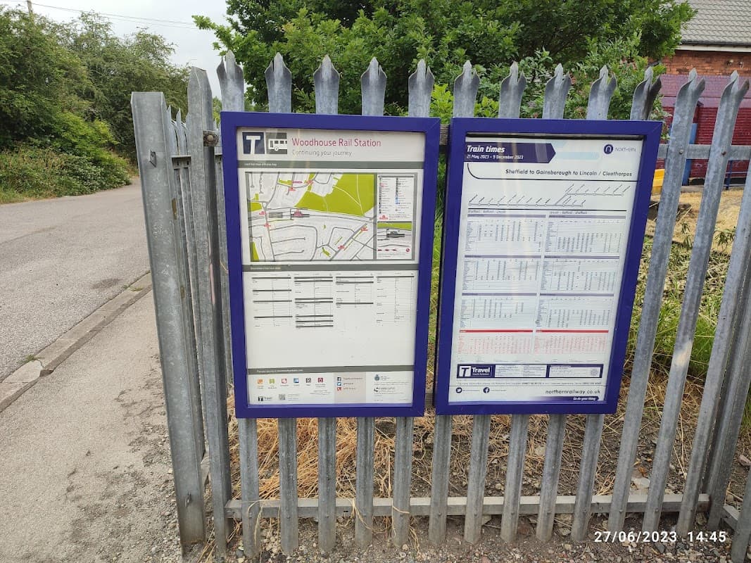 Two information boards at Woodhouse Station Car Park displaying a map and train schedule, surrounded by greenery.