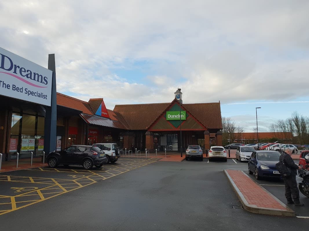 Dunelm store entrance with a red roof, surrounded by parked cars and a cloudy sky in Wortley, Yorkshire.