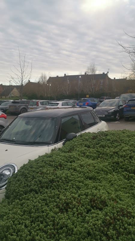 Pay & Display car park at Wortley Beck Health Centre, with parked cars and a bush in the foreground.