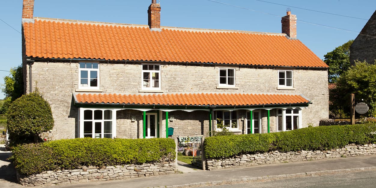 Charming stone building with a red-tiled roof, green accents, and a well-maintained garden in Wrelton, Yorkshire.