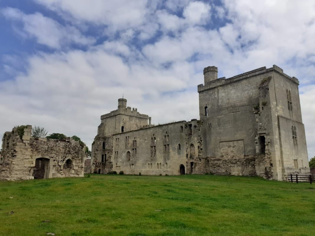 Ruins of Wressle Castle featuring stone walls, towers, and grassy grounds under a cloudy sky.