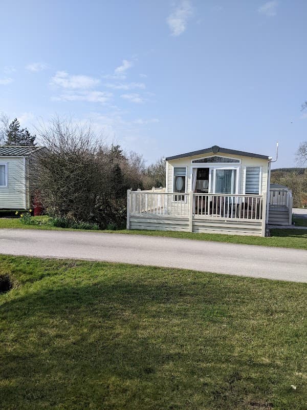Caravan with a wooden deck surrounded by greenery at Crow Trees Caravan Park, Wrigglesworth, Yorkshire.