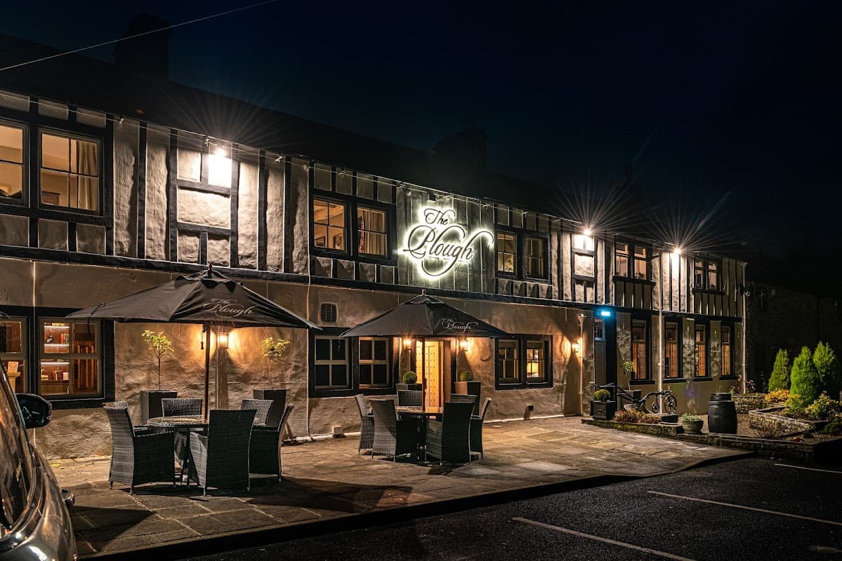 The Plough restaurant at night, featuring outdoor seating, a lit sign, and a traditional Yorkshire stone facade.