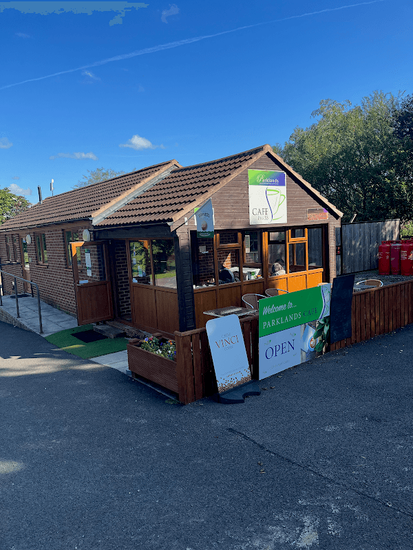 Cozy cafe with wooden exterior, green signage, and outdoor seating in Yafforth, Yorkshire, surrounded by trees.