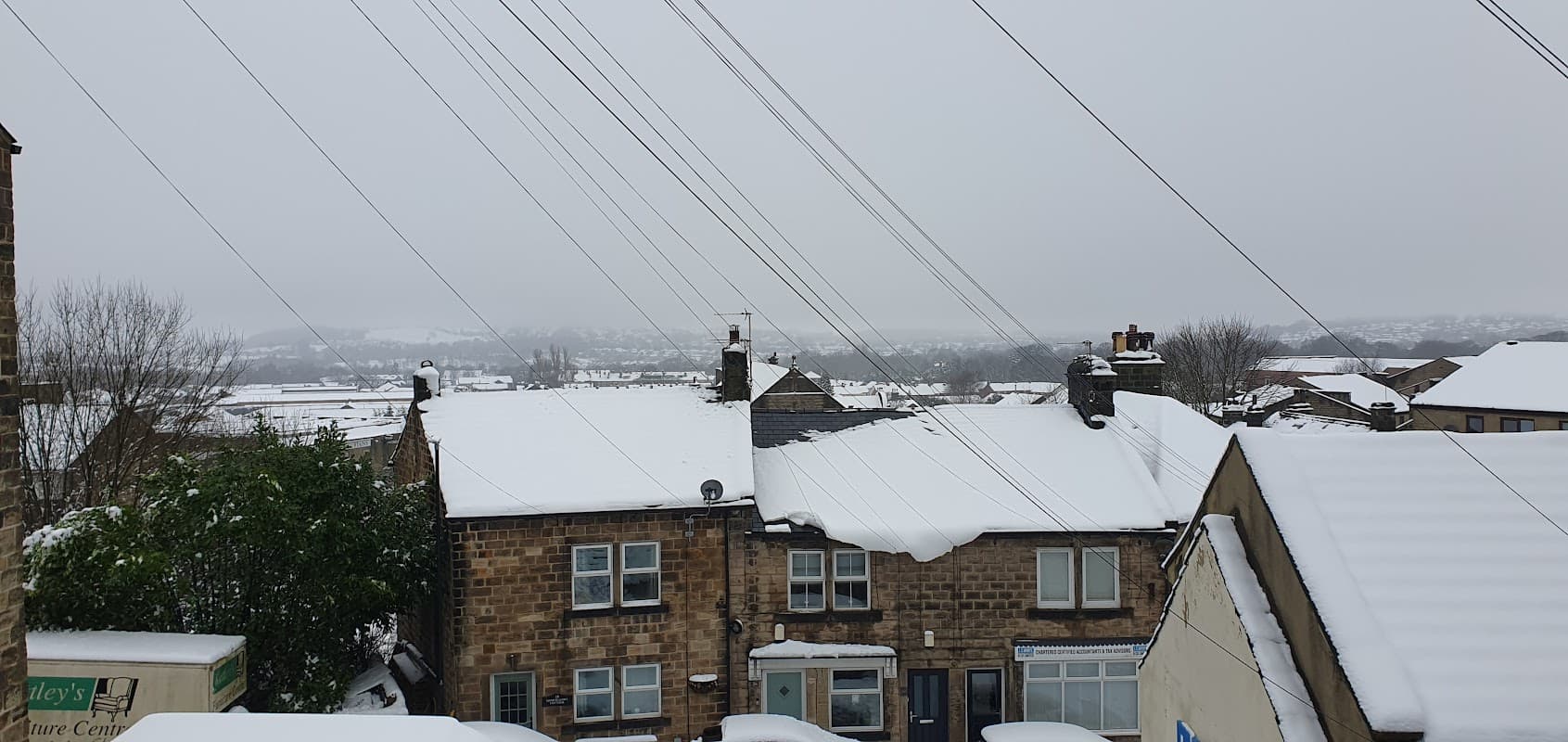 Snow-covered rooftops and streets in a residential area, with power lines and a cloudy sky in the background.