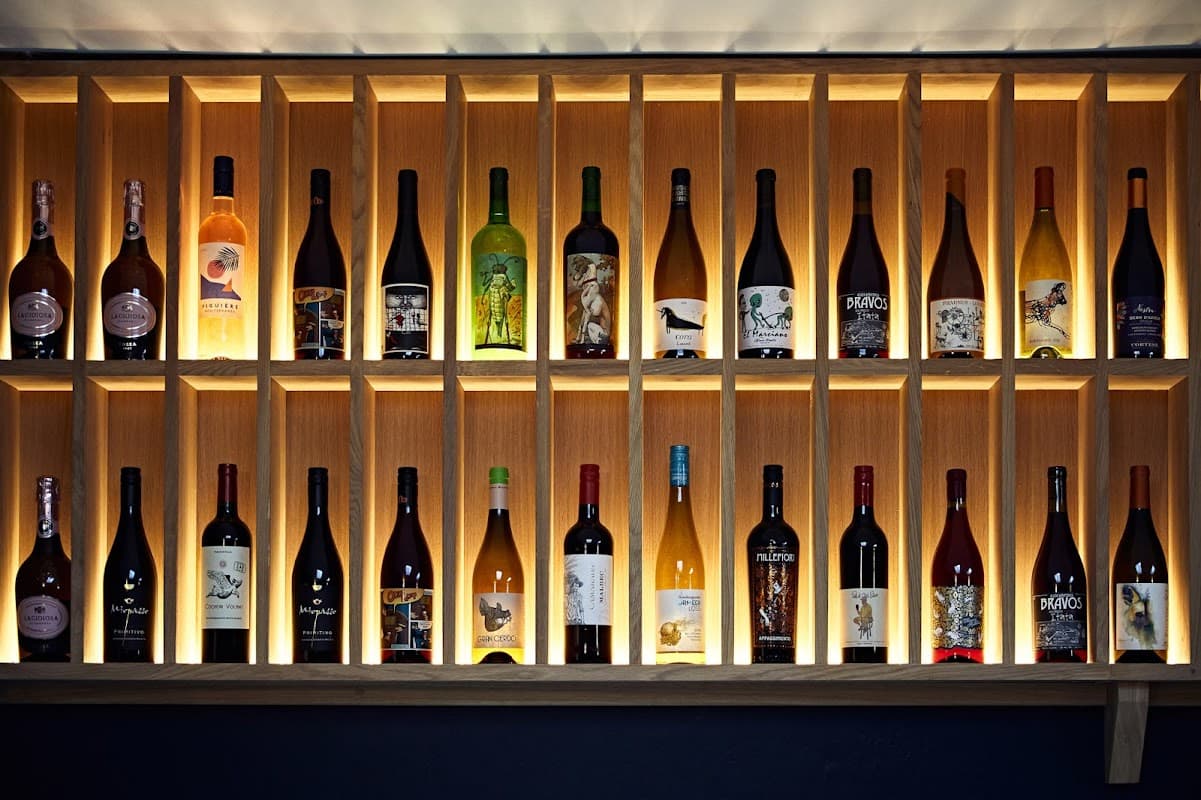 A wooden wine shelf displaying various bottles with unique labels, illuminated by soft lighting.