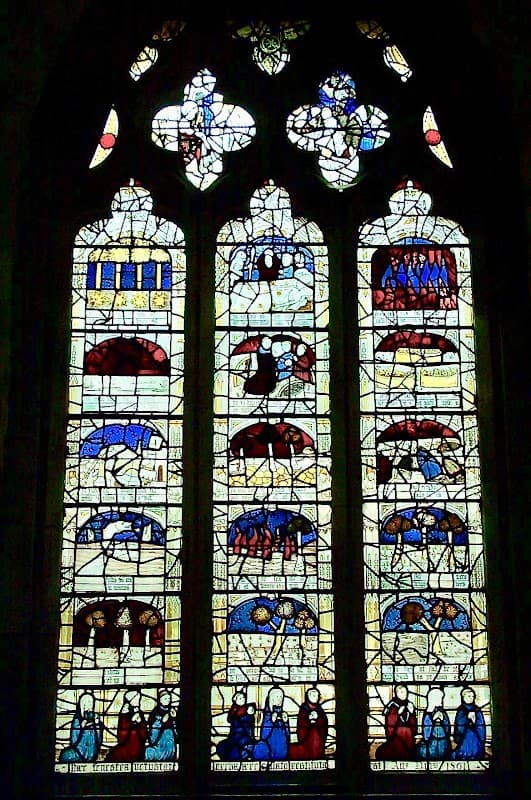 Stained glass window depicting biblical scenes with vibrant colors and intricate designs in a historic church setting.