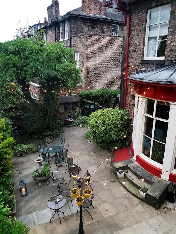 Charming courtyard with tables, chairs, and string lights surrounded by greenery and historic brick buildings.