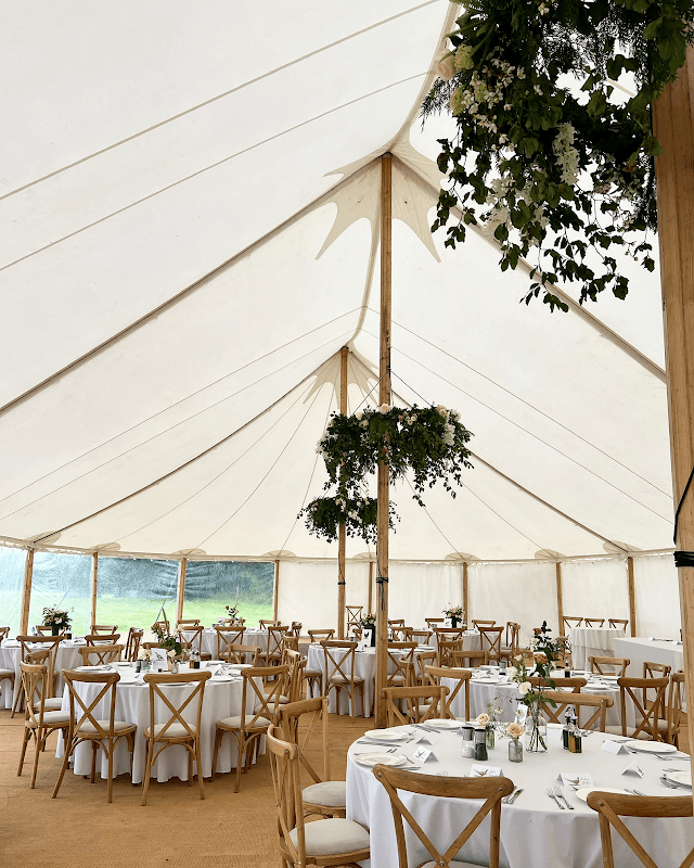 Elegant marquee with round tables, white tablecloths, and greenery hanging from the ceiling, set for an event.