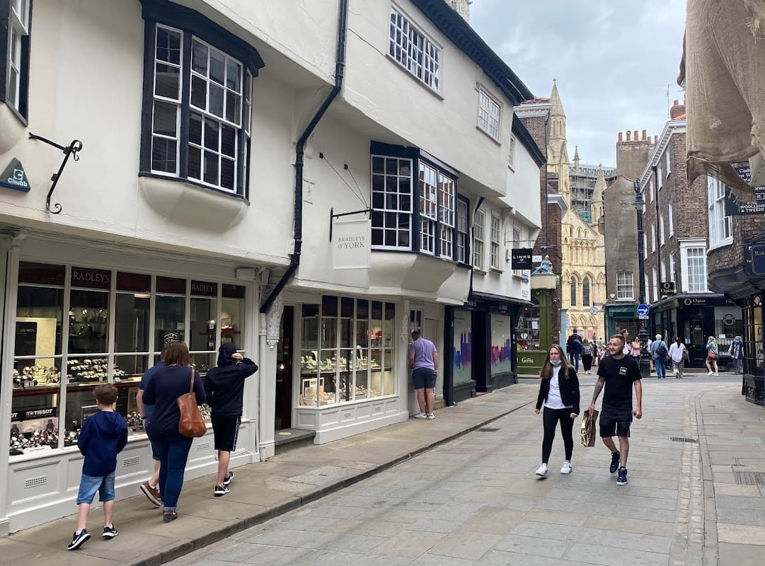 Bradleys The Jewellers storefront with display cases, people walking on a cobblestone street, and York Minster in the background.