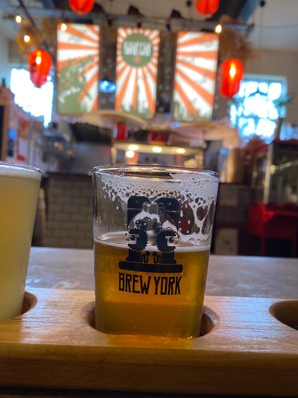 Brew York glass of beer on a wooden flight, with vibrant red lanterns and colorful banners in the background.