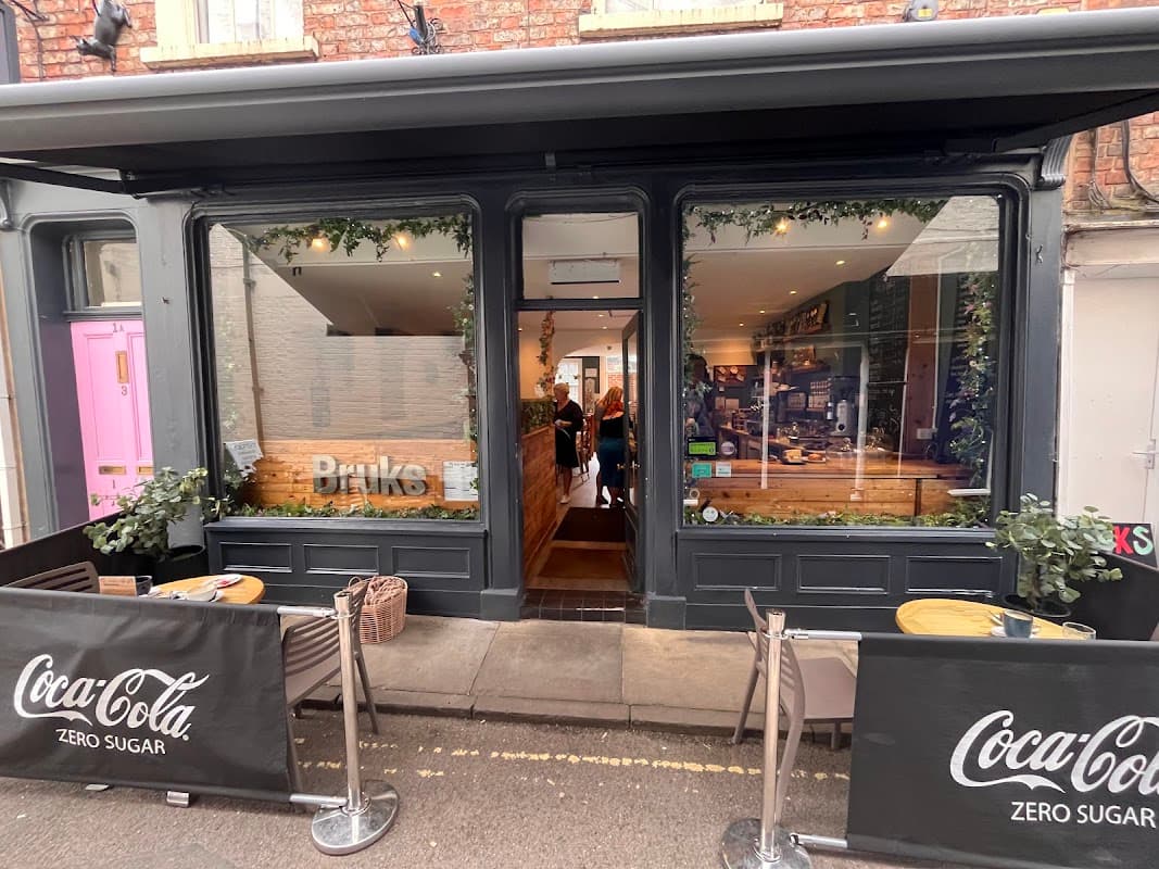 Charming cafe entrance with wooden decor, plants, and outdoor seating, inviting patrons inside.