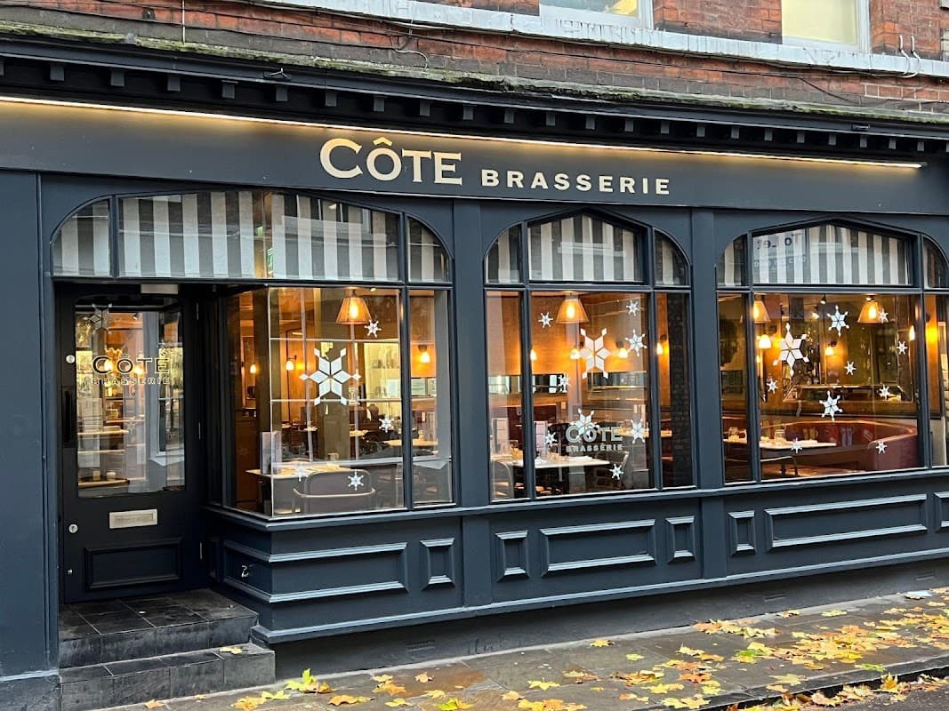 Côte Brasserie restaurant exterior with large windows, warm lighting, and decorative snowflake designs.