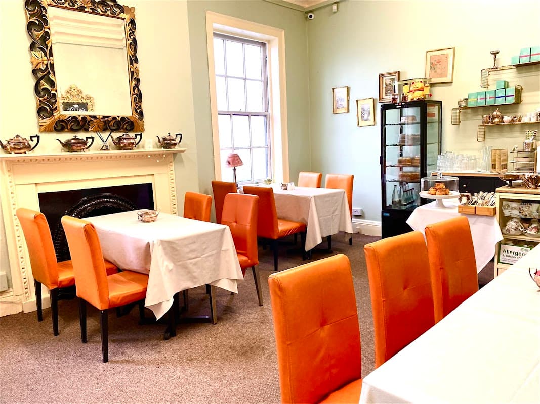 Cozy café with orange chairs, white tablecloths, a decorative mirror, and a display case of pastries.
