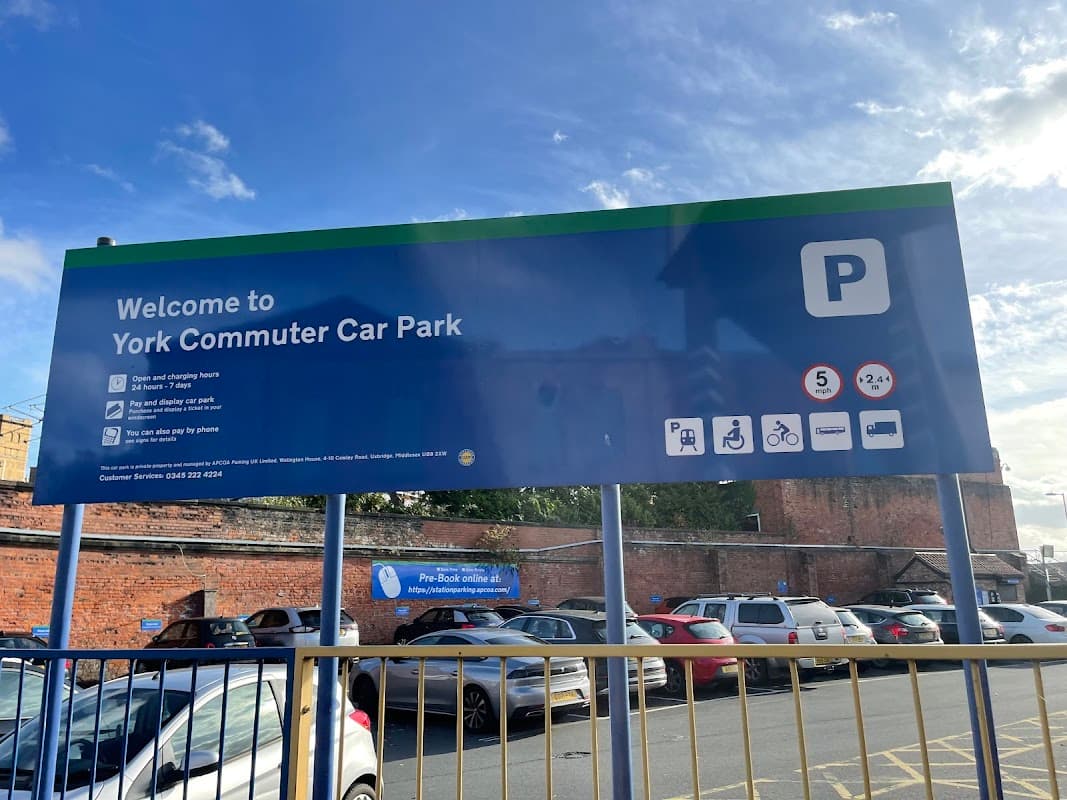Welcome sign for York Commuter Car Park with parking details, hours, and contact information. Cars visible in foreground.