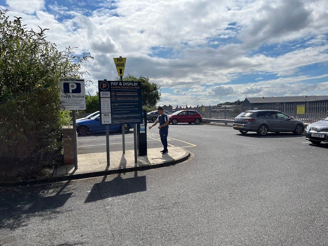 Pay and display parking sign with a person near cars and a cloudy sky in Carlisle Street Car Park, York.