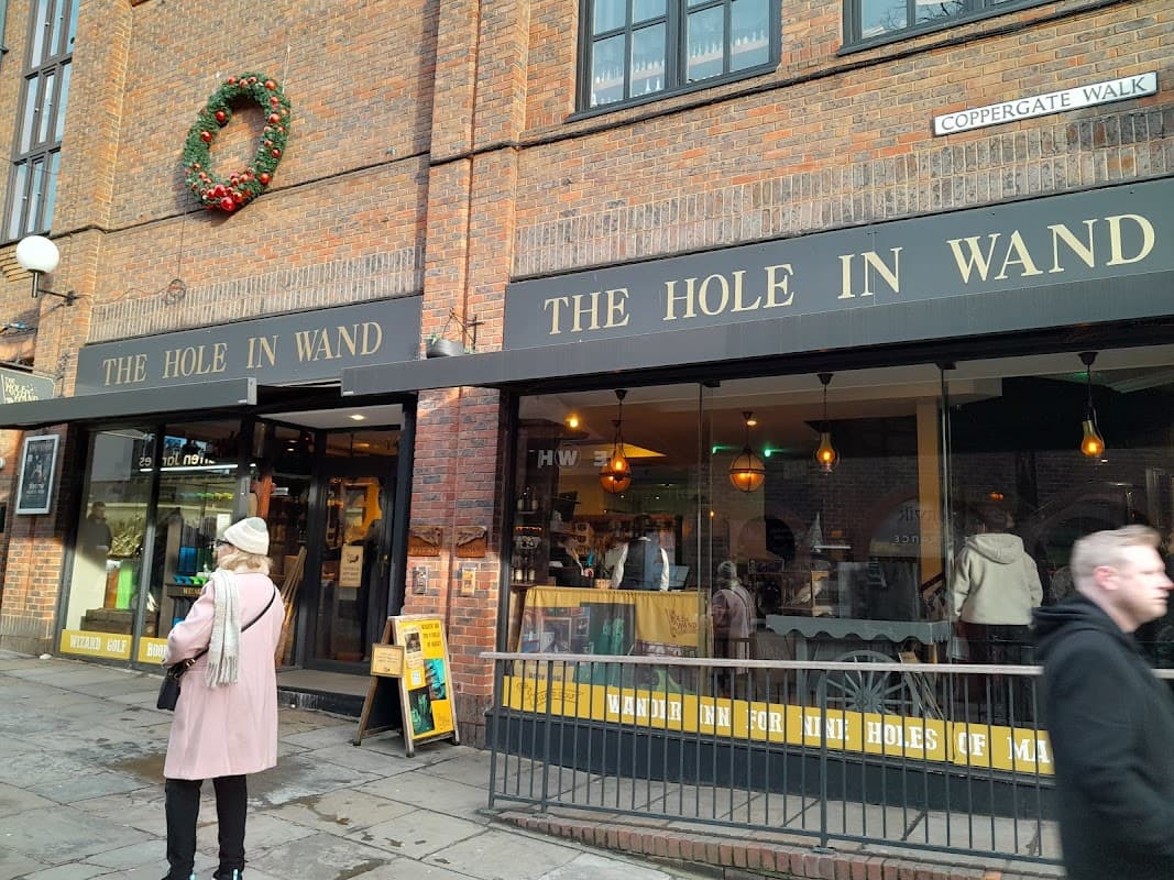 Shopfront with "The Hole in Wand" signage, festive wreath, people walking by, and a cozy interior visible through the windows.