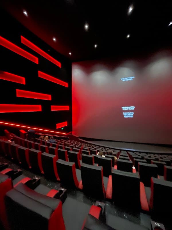 Modern cinema interior with red accents, empty rows of plush black seats, and a large blank screen at the front.