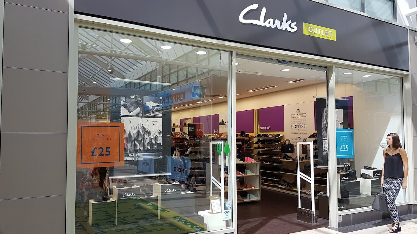 Clarks Outlet storefront with large sale signs, showcasing shoes and a bright, modern interior.